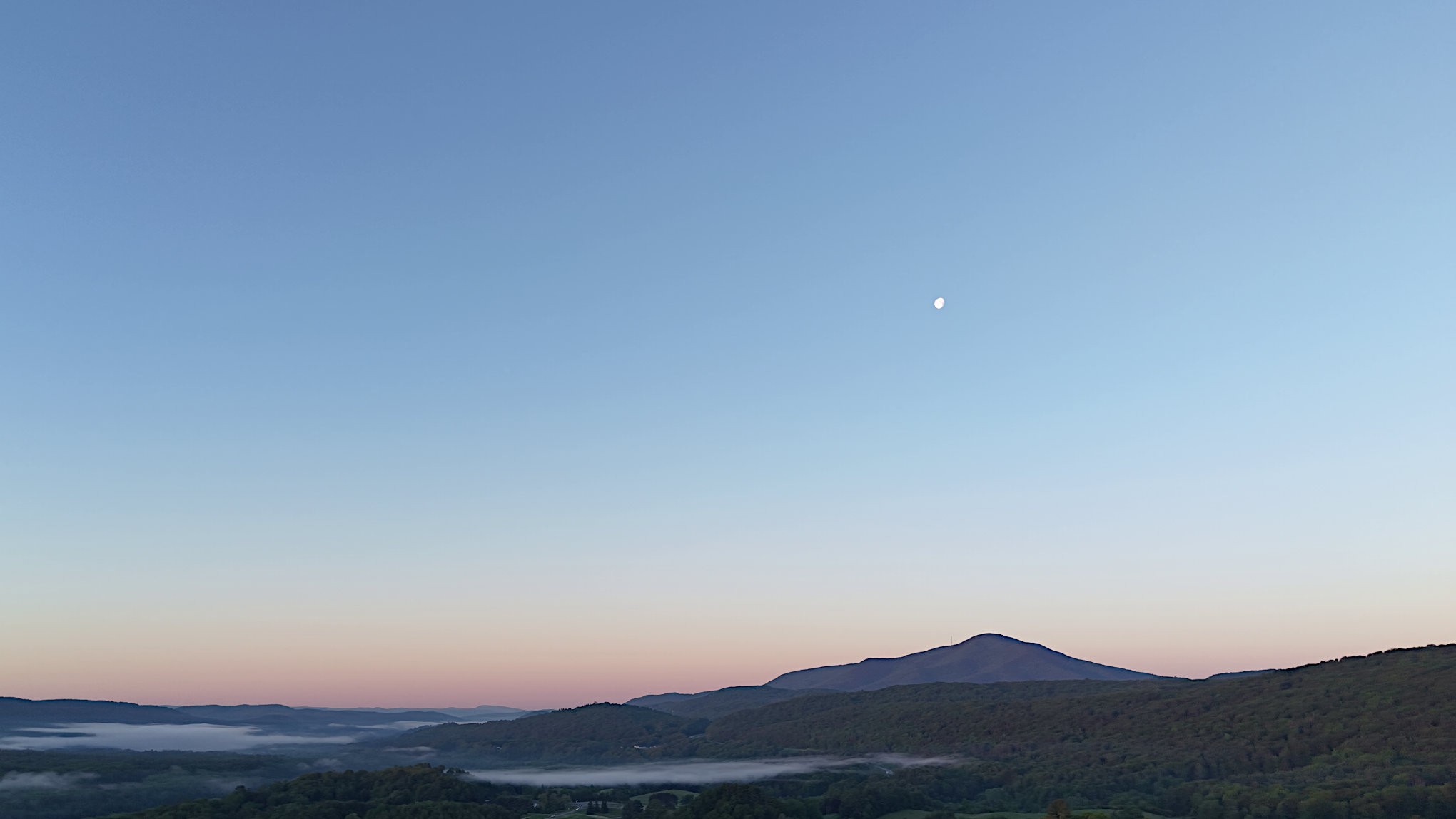 Fog pooled in the valley below Mount Ascutney at dawn with the moon still up