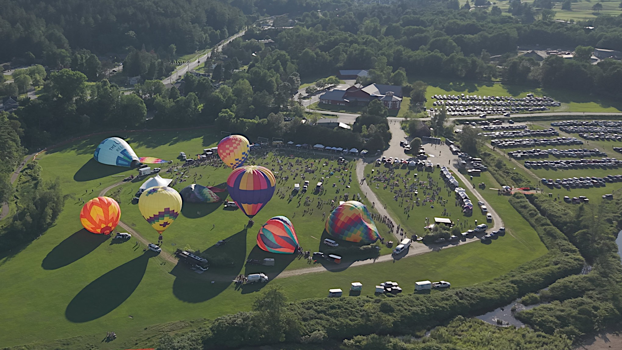 Balloons inflating on the festival field with crowds and shadows stretched long