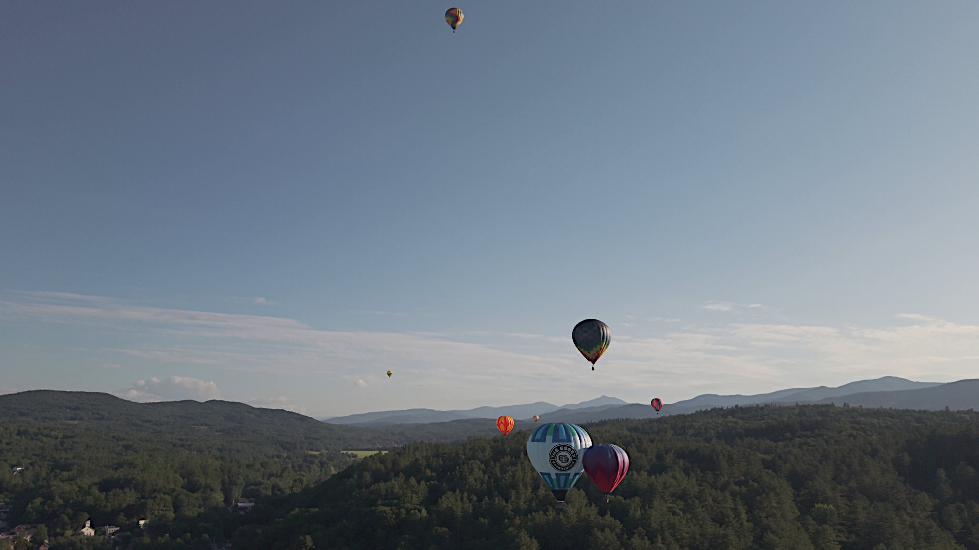A dozen hot air balloons scattered across the sky over the Green Mountains