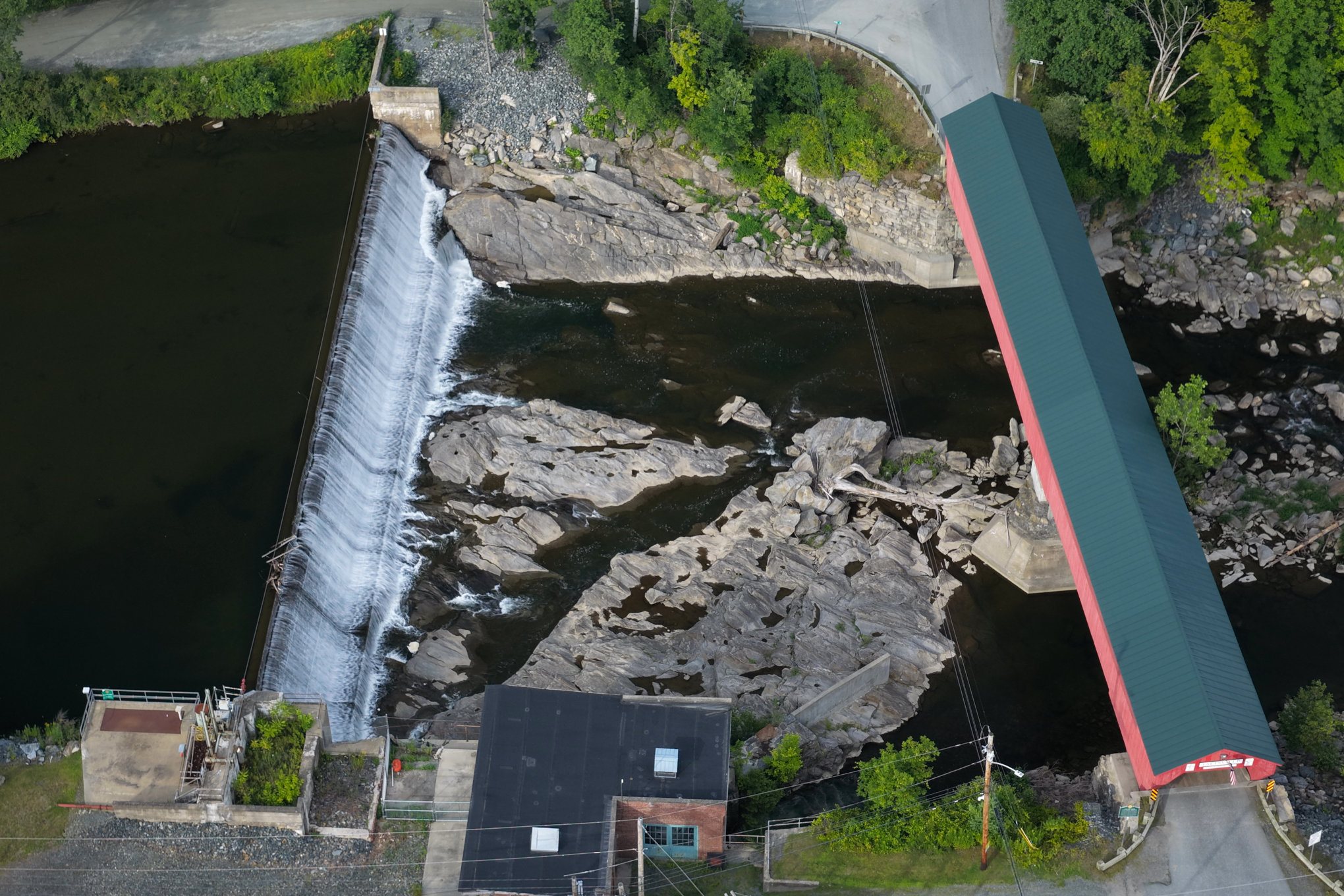 The Taftsville dam spilling white beside the red covered bridge, seen straight down