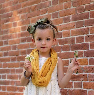 Portrait of a child holding wildflowers against a brick wall